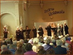 Devant le public, le représentant d'Emmaus (à gauche), et le groupe vocal